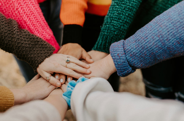 Volunteers' hands stacked together in colourful jumpers.